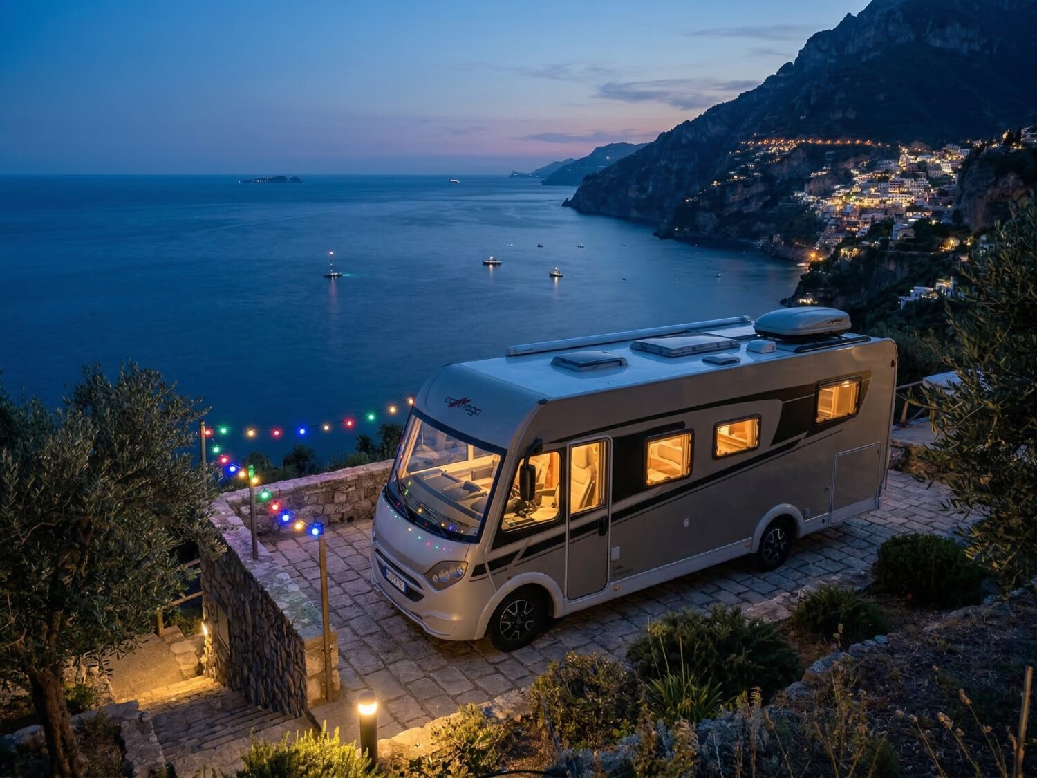 Autocaravana con vistas al mar por la noche con luces y pueblo iluminado, viaje en camper con Libertad Sobre Ruedas en la costa